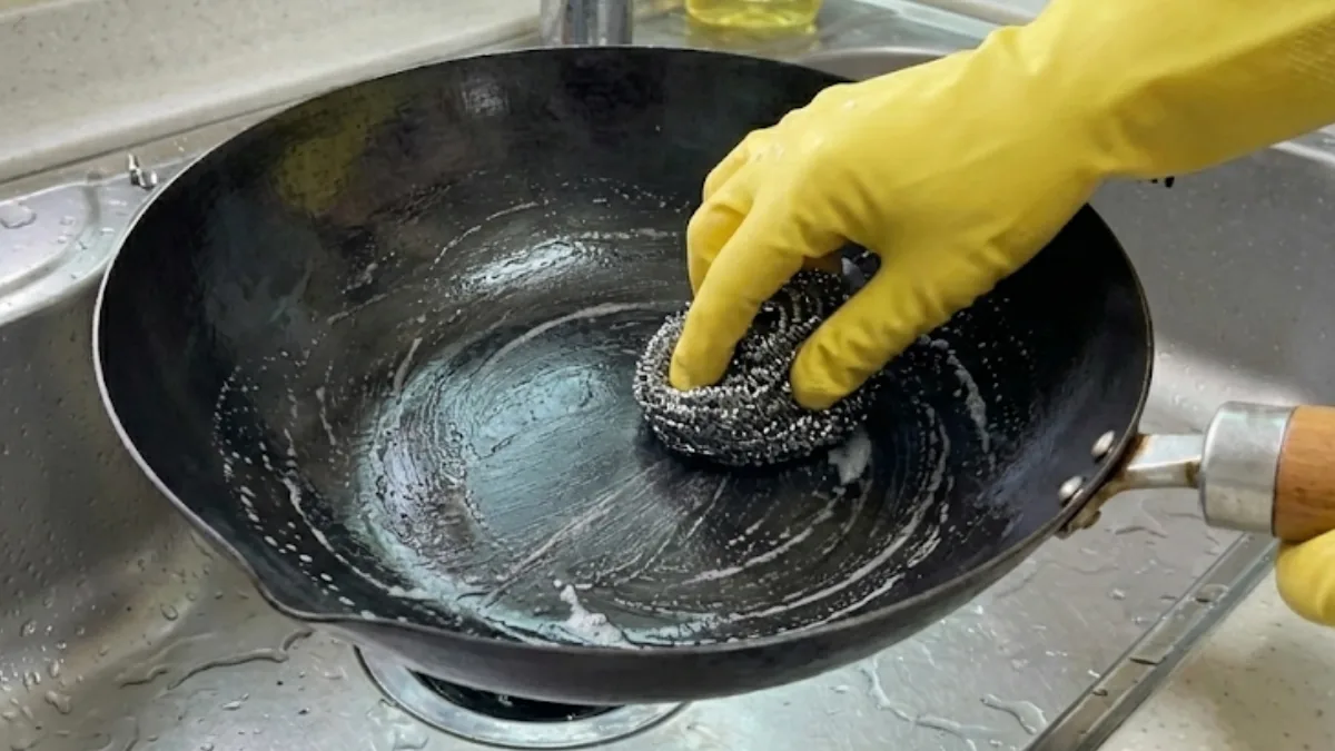 Scrubbing a Japanese iron frying pan with a steel wool pad to remove rust, showing the restoration process