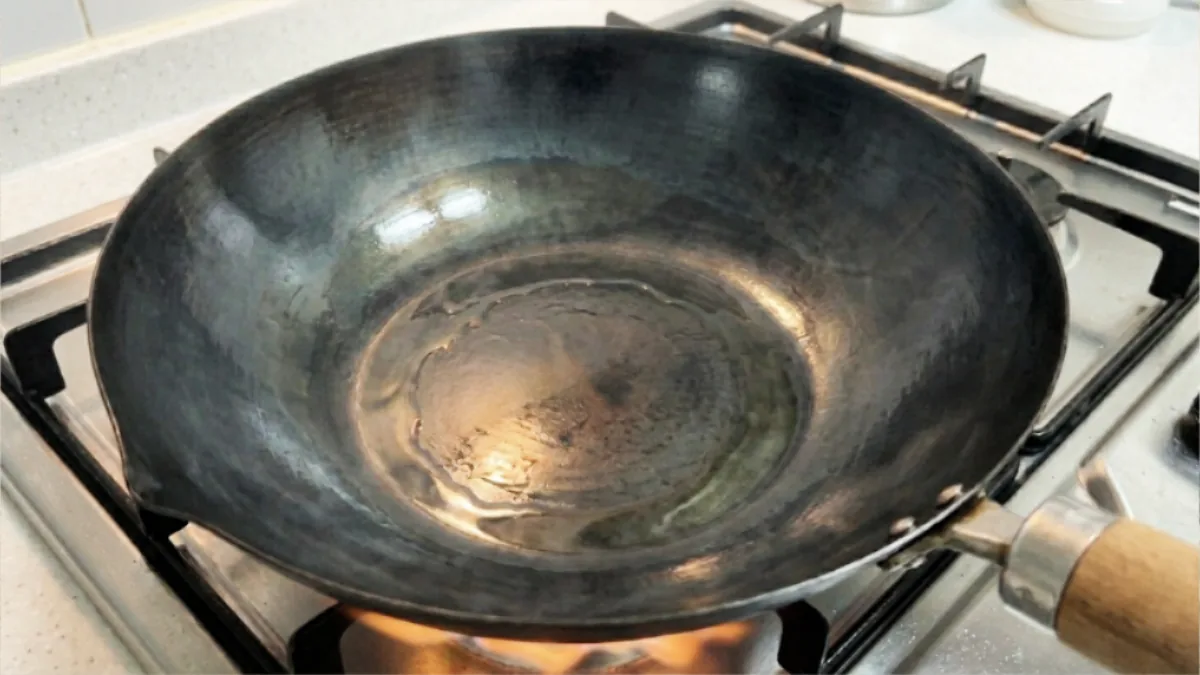 Pouring oil into a Japanese iron frying pan for initial seasoning, showing the process of coating the entire cooking surface