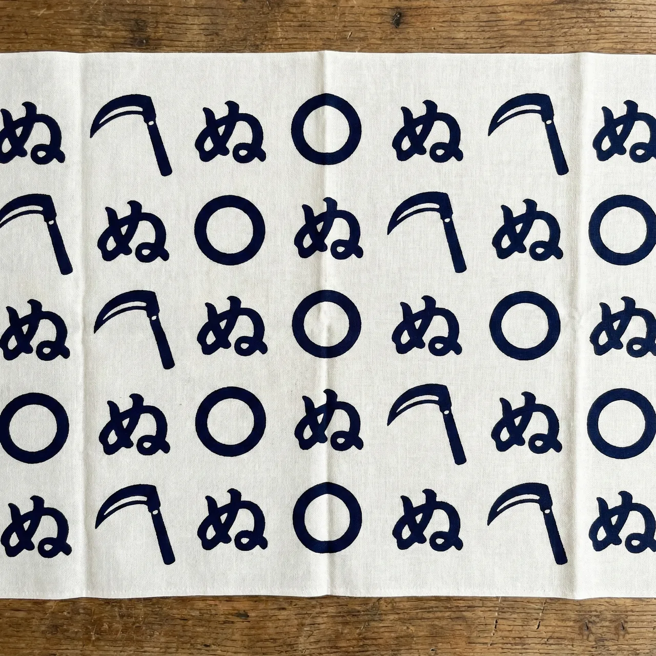 鎌と輪と「ぬ」の文字がデザインされたユニークなかまわぬ柄の手ぬぐい